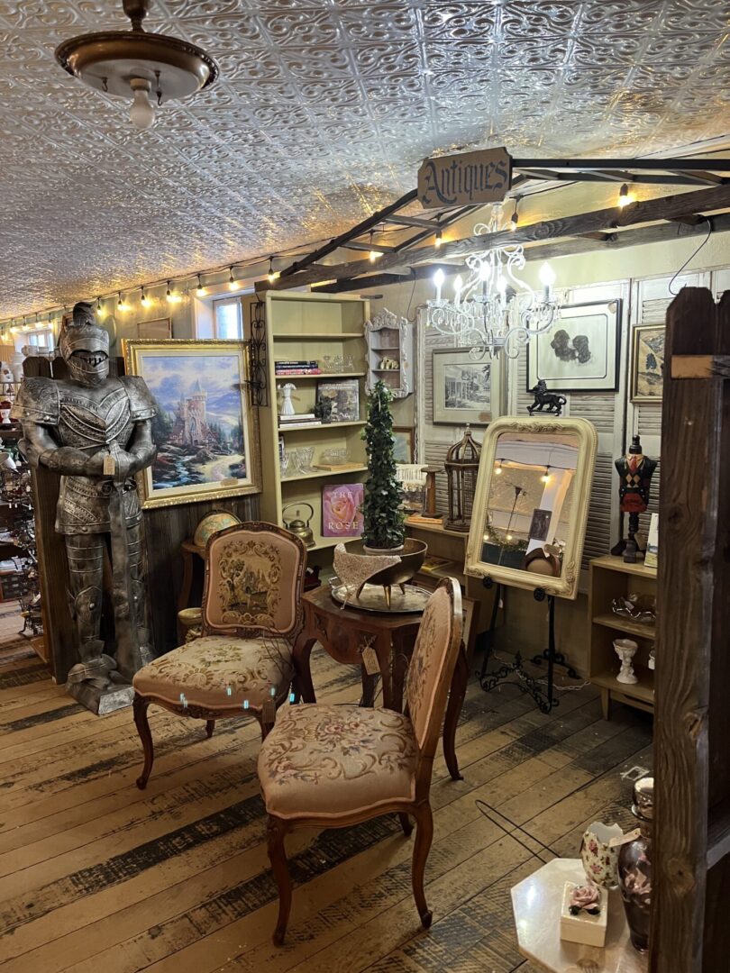 A cozy vintage room with antique chairs, framed pictures, and a medieval knight suit.